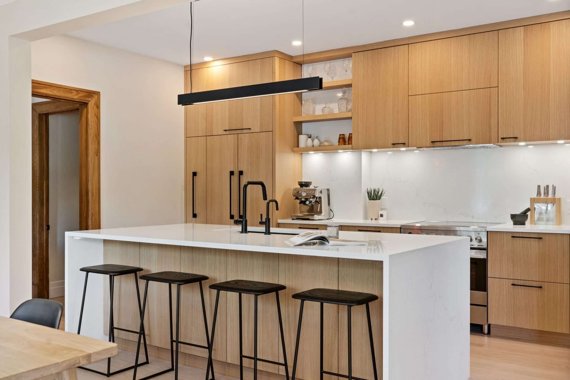 Cuisine contemporaine avec armoires en bois clair, îlot blanc épuré et luminaires design, illustrant un style moderne et chaleureux.