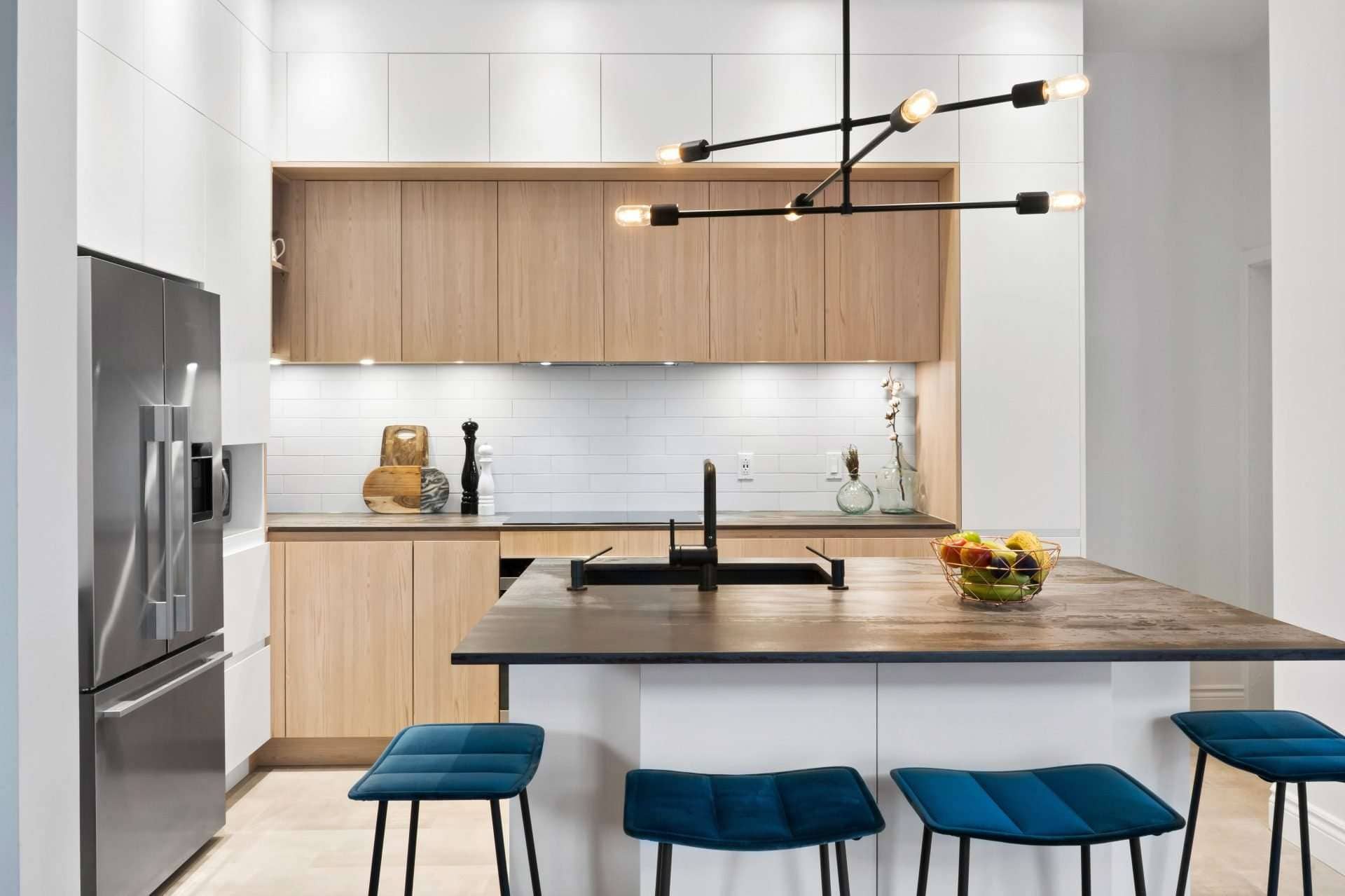 Cuisine moderne avec armoires minimalistes en bois clair, îlot avec comptoir foncé et luminaires graphiques, offrant un design épuré et fonctionnel.